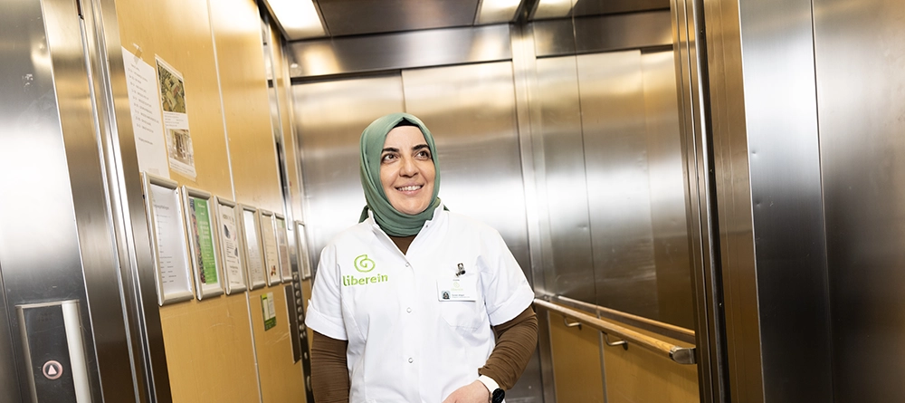 Zorgmedewerker in wit uniform en hoofddoek in de lift van een zorginstelling