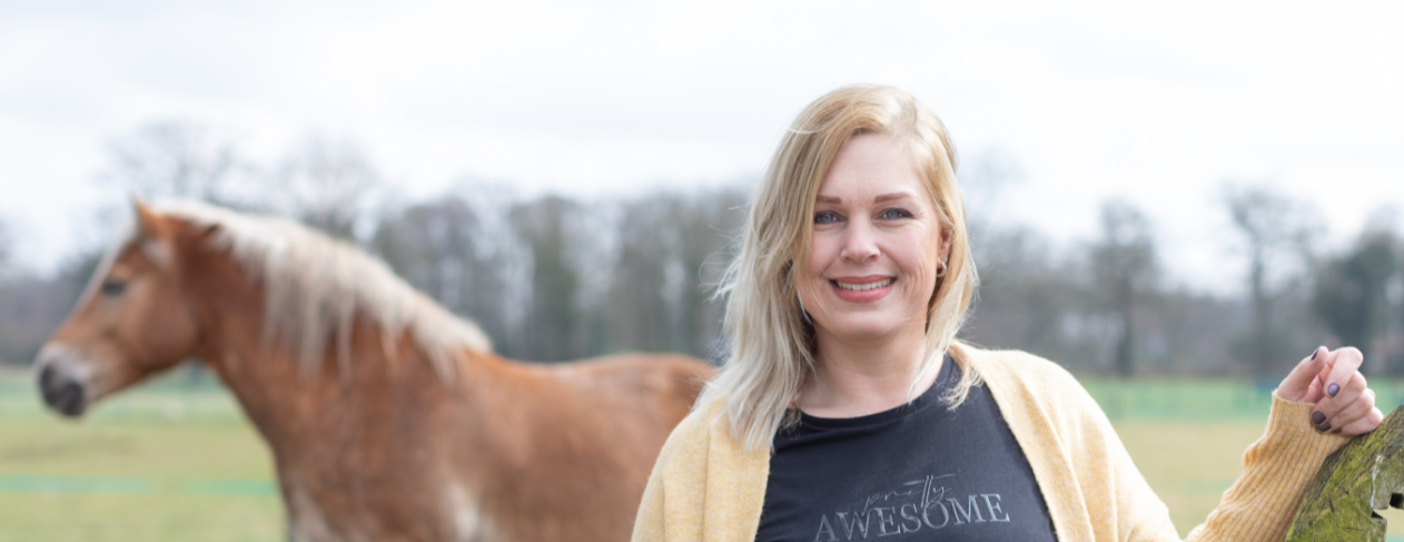 Vrouw glimlacht buiten met een paard op de achtergrond