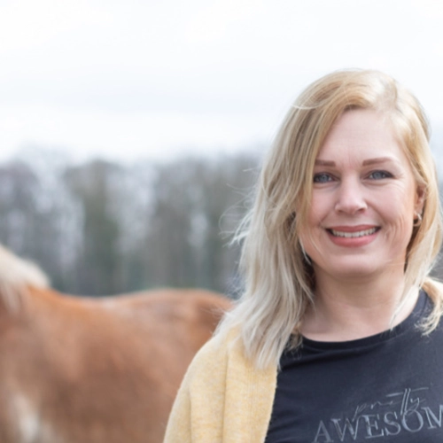 Vrouw glimlacht buiten met een paard op de achtergrond