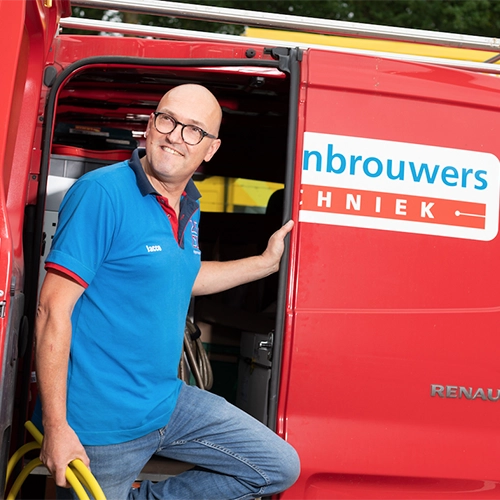 Technisch medewerker stapt uit rood busje van Hoppenbrouwers Techniek