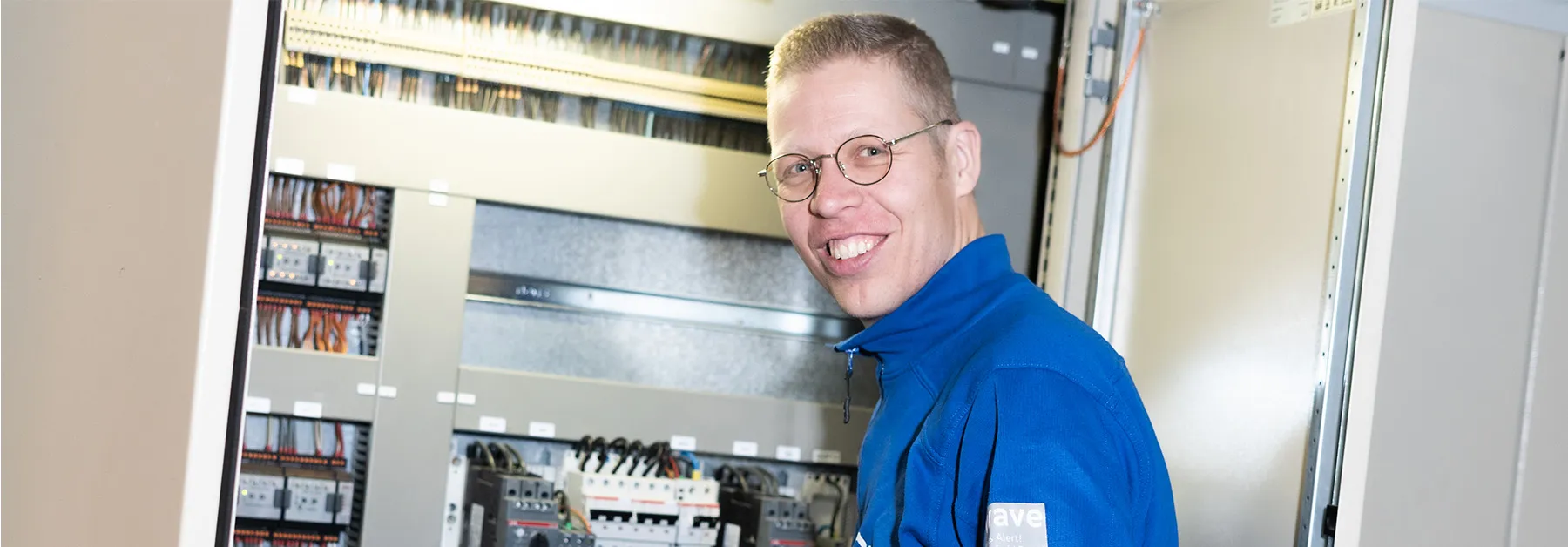 Technisch medewerker naast schakelkasten en bedrading tijdens werk in de technieksector.