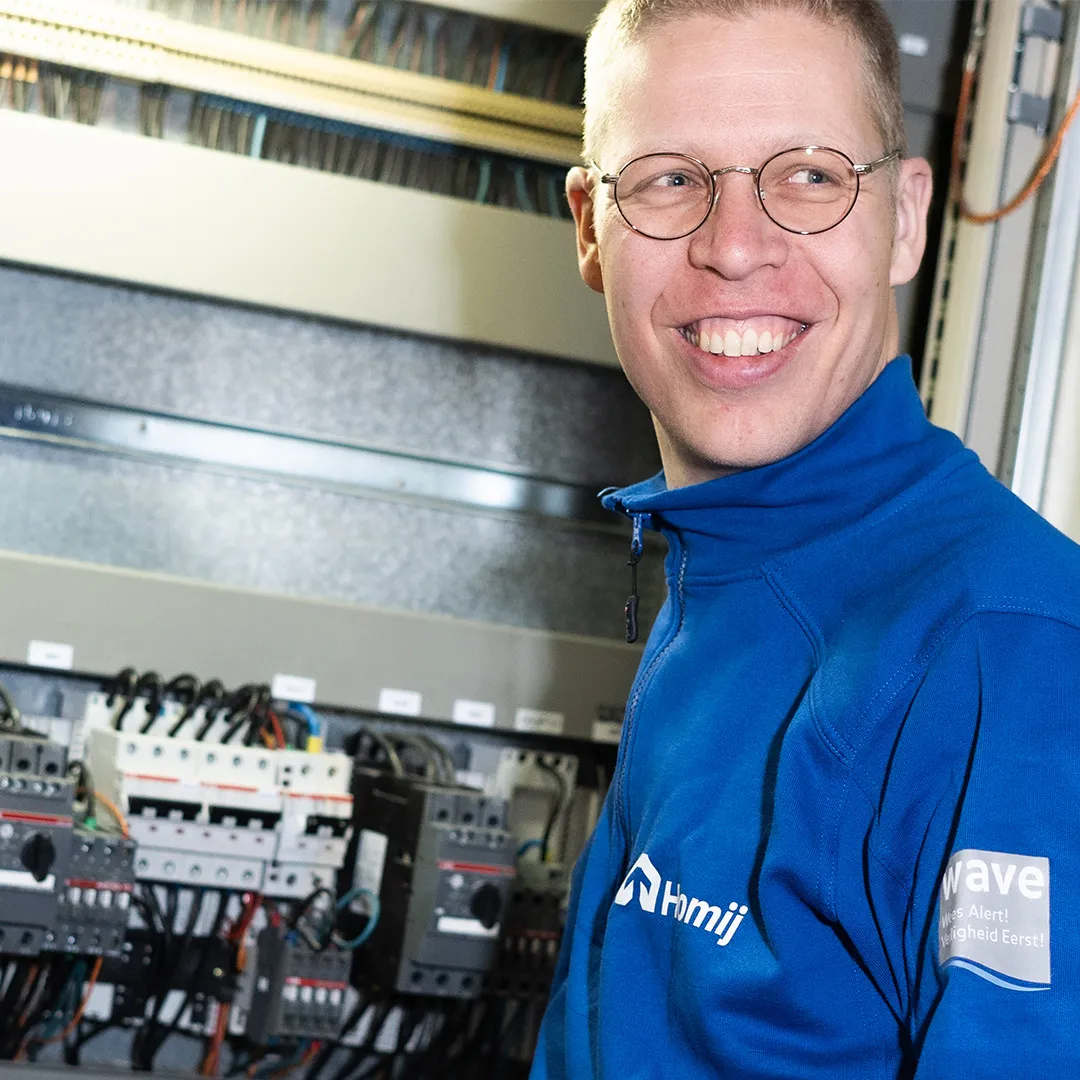 Technisch medewerker naast schakelkasten en bedrading tijdens werk in de technieksector.